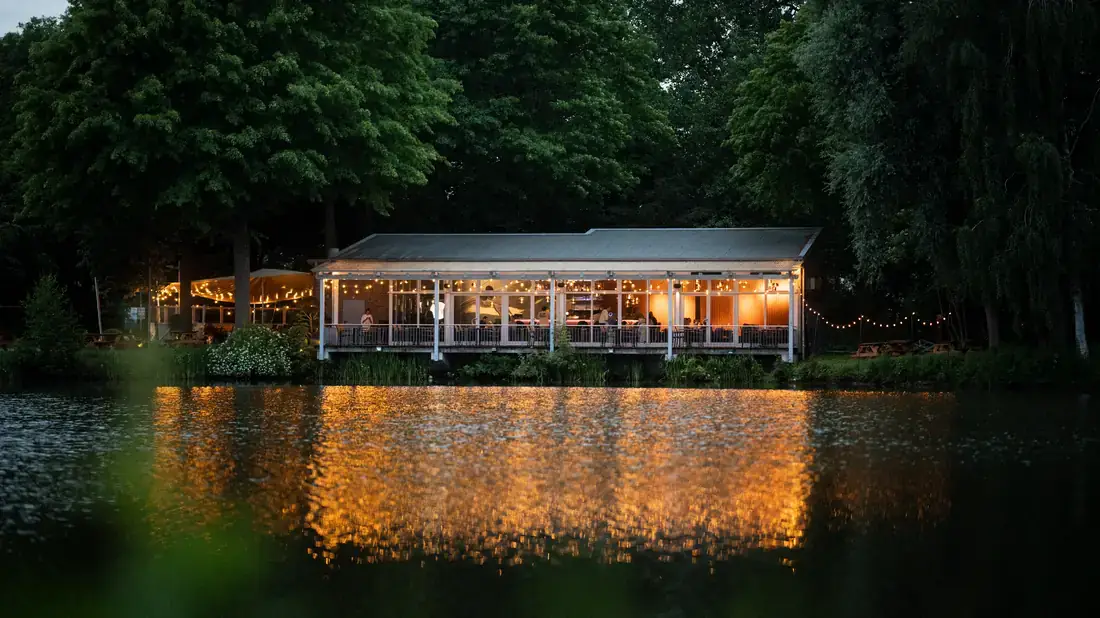 Harry's – Haus am See am Abend mit Lichterketten über dem Wasser